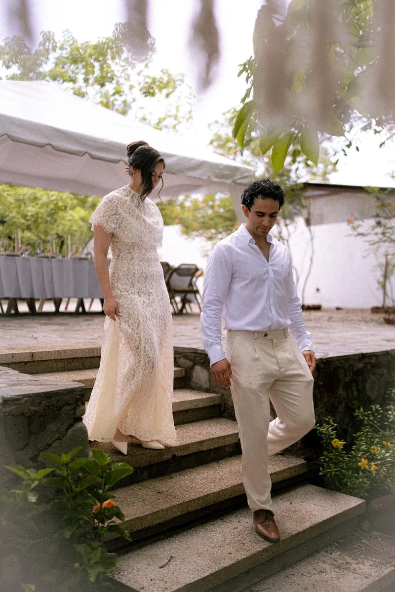 Gus y Karla bajan juntos unas escaleras hacia el jardín, ella marcando el paso, en su boda